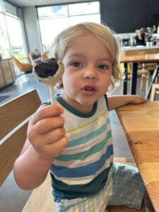 Toddler boy holding a cake pop sitting at a table in a restaurant in Jacksonville, FL