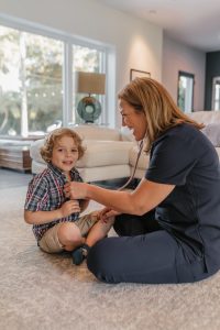 Female NNP is in First Call Pediatric scrubs, while 4-year-old boy pediatric patient receives physical exam from pediatric team member with stethoscope during in-home visit in San Marco neighborhood, Jacksonville, FL.