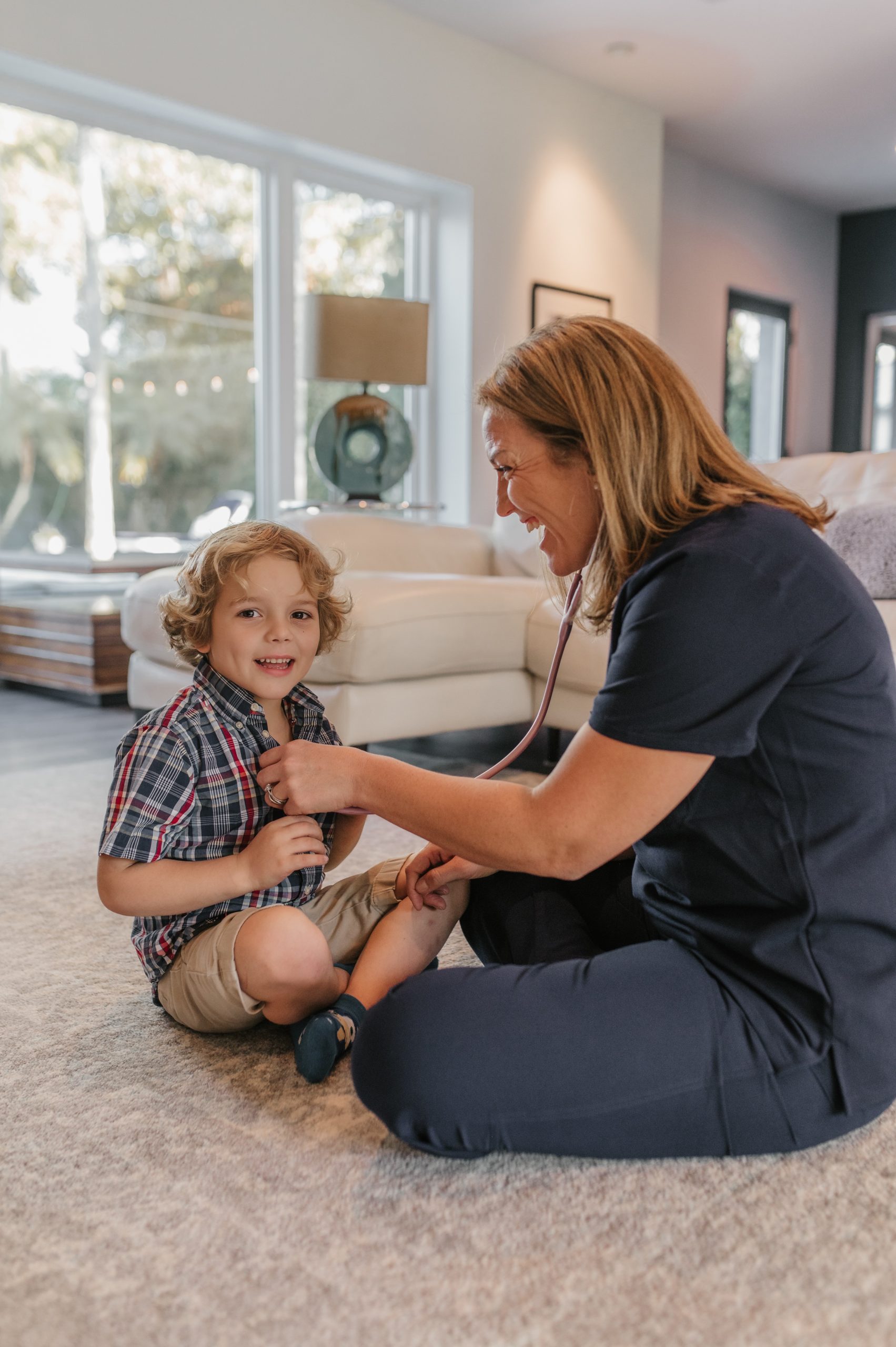 Female NNP is in First Call Pediatric scrubs, while 4-year-old boy pediatric patient receives physical exam from pediatric team member with stethoscope during in-home visit in San Marco neighborhood, Jacksonville, FL.