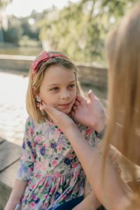 Female pediatric care provider preforming physical exam, with hands pressing under 6-year-old girl’s ear/upper throat area, outside at child’s home in San Marco neighborhood in Jacksonville, Fl.