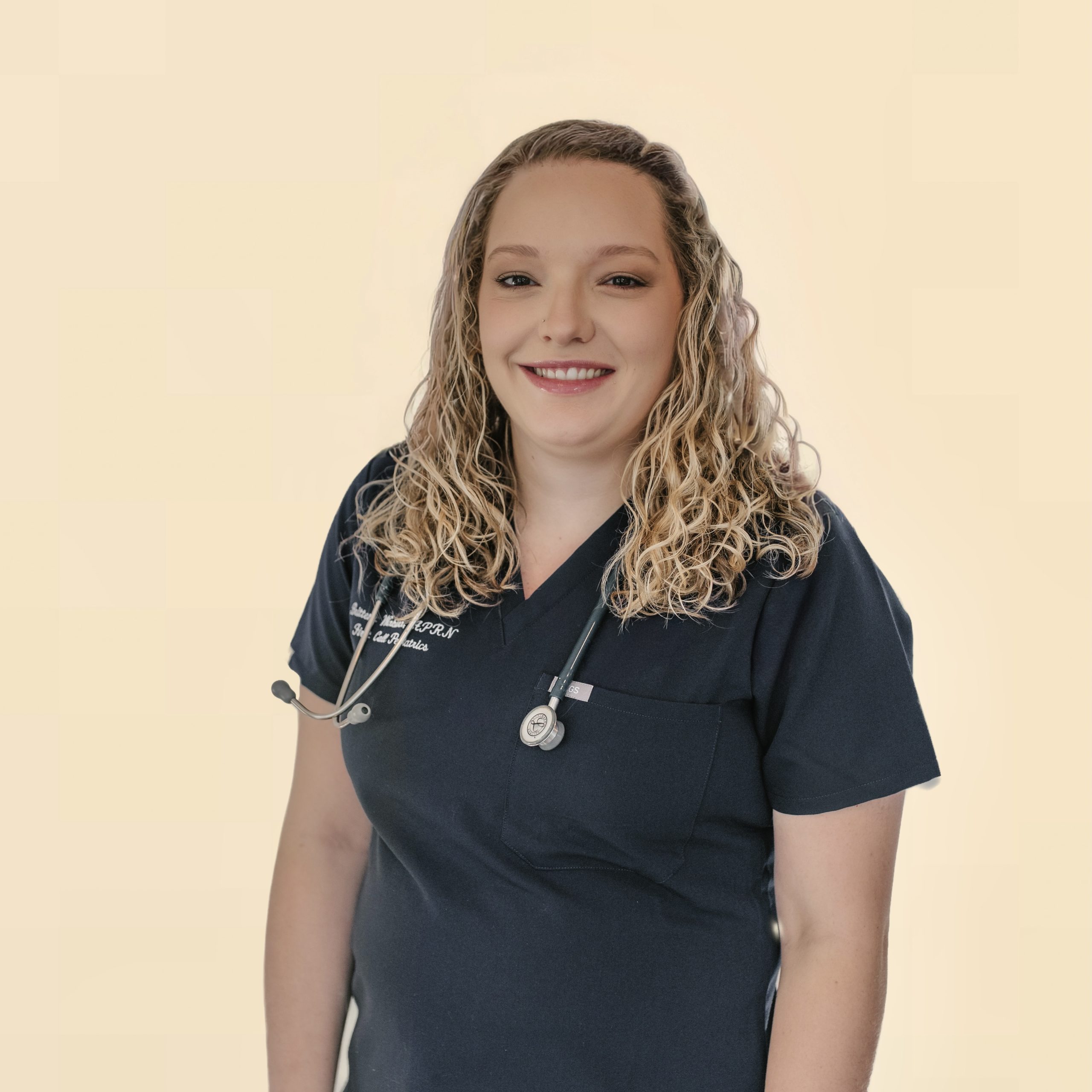 • Blond, curly haired female PNP in First Call Pediatric Scrubs, smiling, wearing a stethoscope, in Jacksonville, Fl.