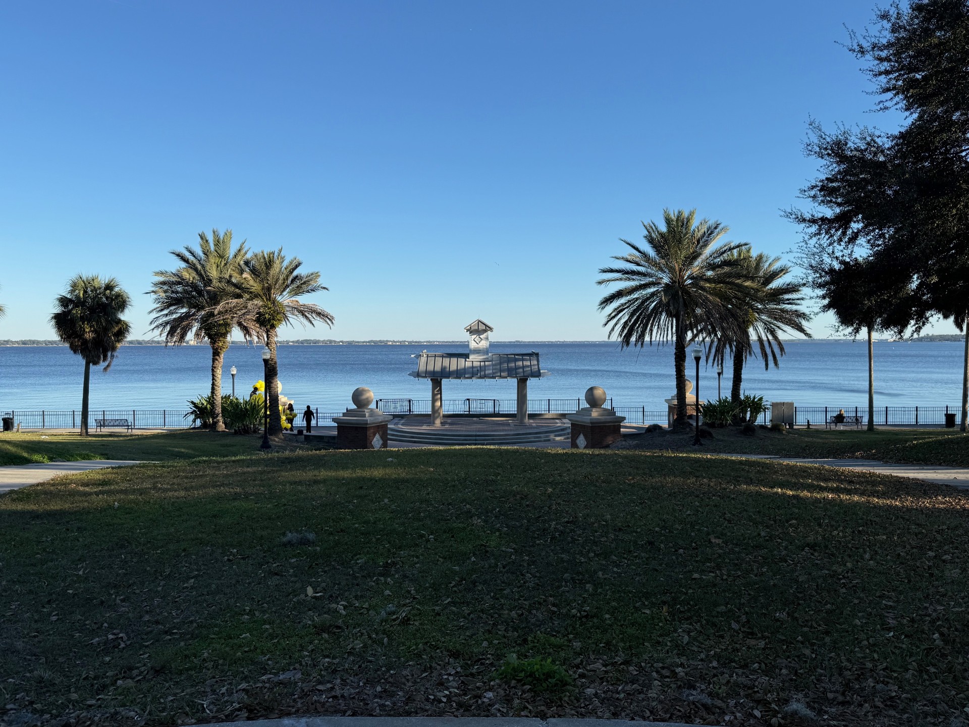 Stockton Park overlooking the St. Johns River in Ortega, Jacksonville, FL, with the gazebo centered, with two brick pillars with balls on top that have connecting brick seating that curve around the gazebo, with two palm trees on the left and right side.