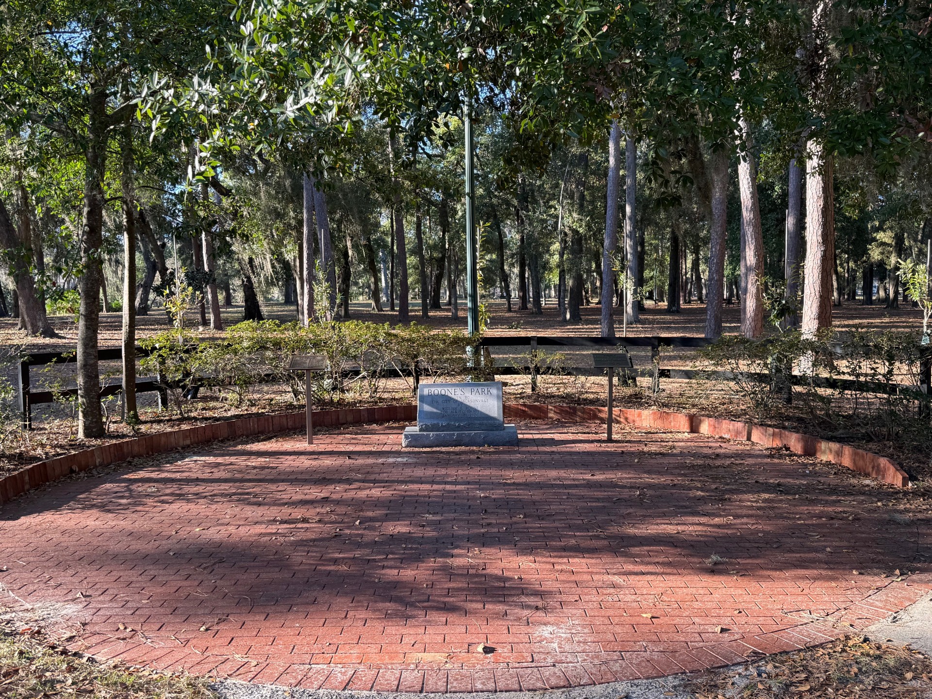 Boone Park stone slab in honor of the founders, with bricks laid in a circle surrounding it, with a half wooden fence behind it, with the woods in the background in Avondale, Jacksonville, FL
