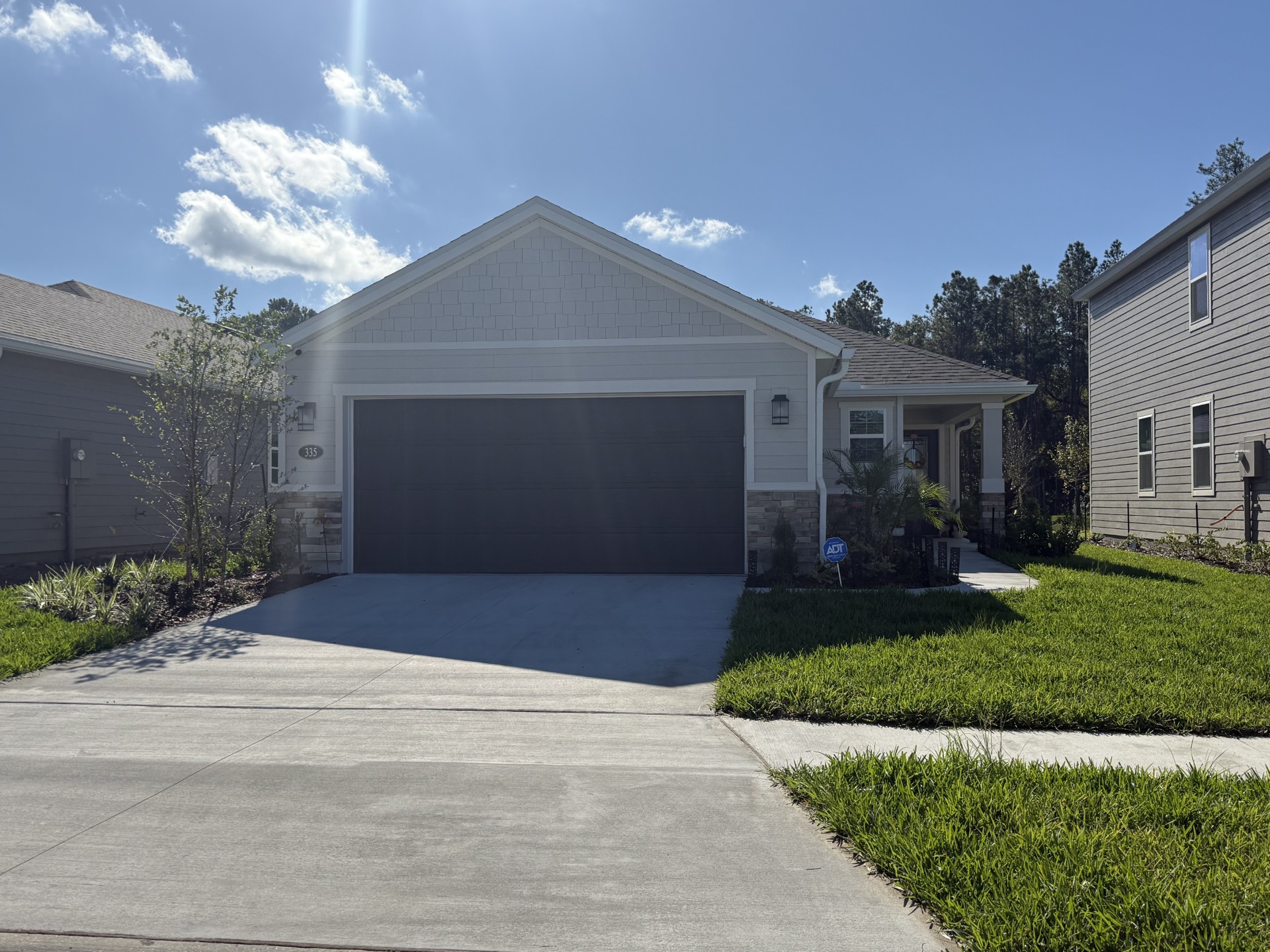 A driveway that leads up to a white house with brick on the bottom section of the house, with a tree to the left and a walkway that leads up to the front door with a garden to the right of it, in Nocatee, FL.