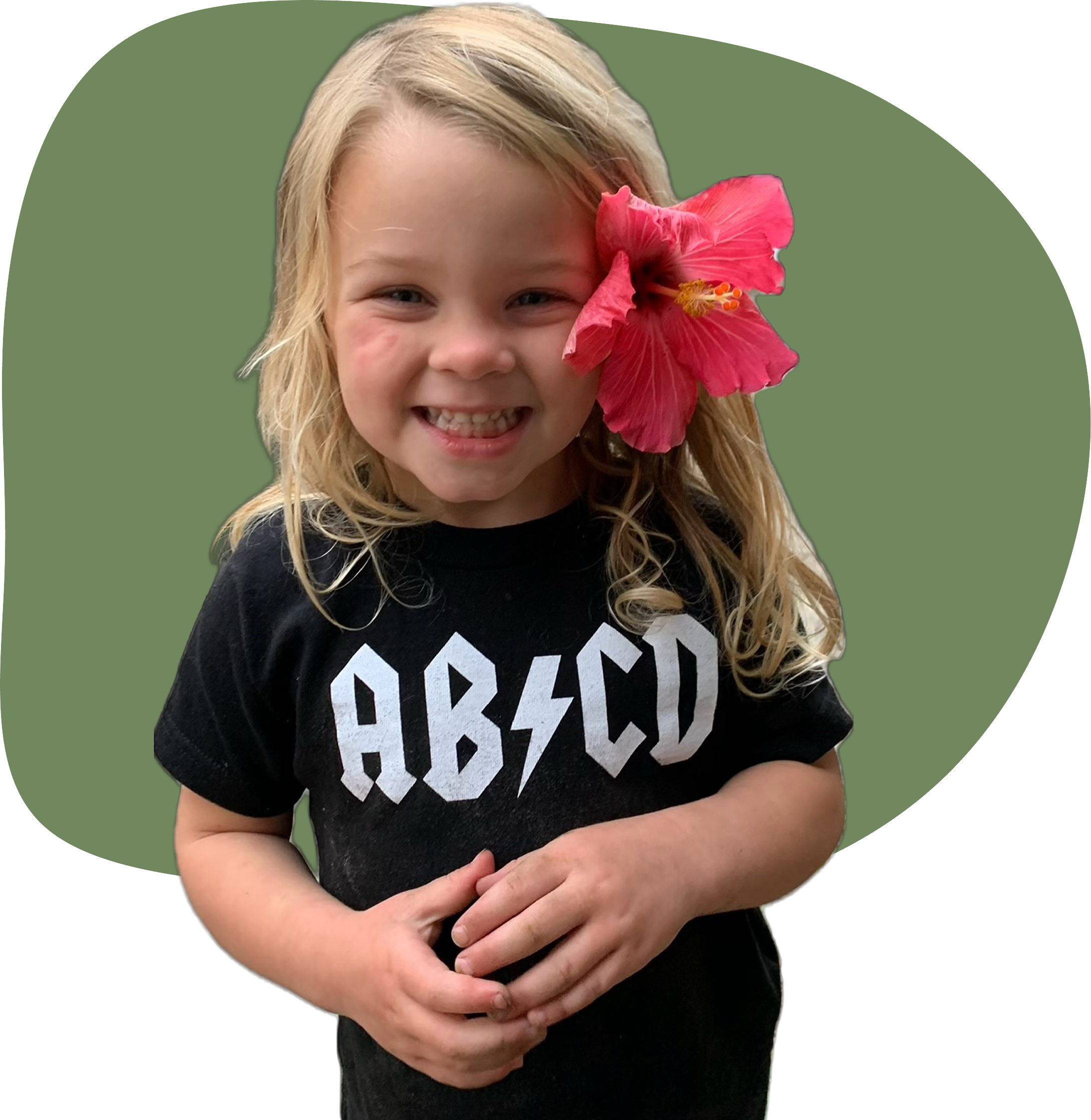 2-year-old girl smiles at camera with hibiscus in her hair, wearing a black t-shirt and jeans at home, in Ortega, Jacksonville, Fl