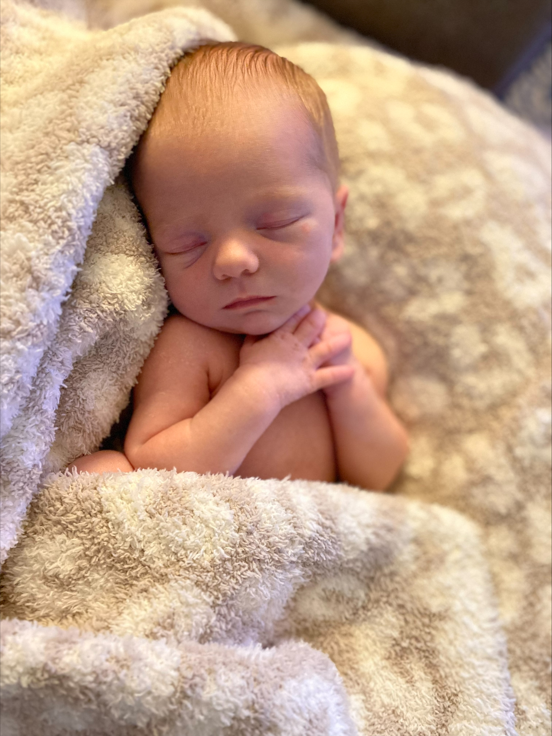 Newborn sleeping with arms by neck, surrounded by an off-white fluffy blanket, at Jacksonville Beach, FL