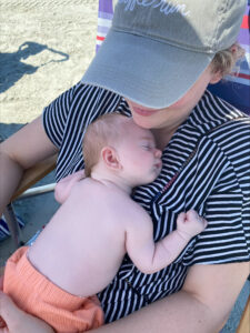 Newborn sleeping, wearing orange shorts, on a woman's chest, who is wearing a striped bathing suit, at Jacksonville Beach, FL