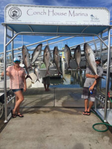 Britteny, pediatric Np, standing to the left in a pink shirt with 9 fish strung up between her and a male on the left ina grey shirt and black shorts, with boats in the background, in Jacksonville, FL