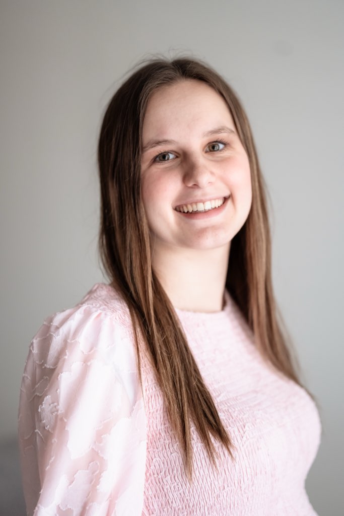 Woman, smiling at camera, with light brown hair, wearing a long sleeve pink shirt.